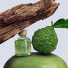 Citrus Wood Signature Scent oil bottle beside a fresh bergamot and a piece of weathered wood