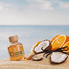 Cocoa Beach Signature Scent oil bottle in the sand by the ocean with sliced oranges, coconut and vanilla beans