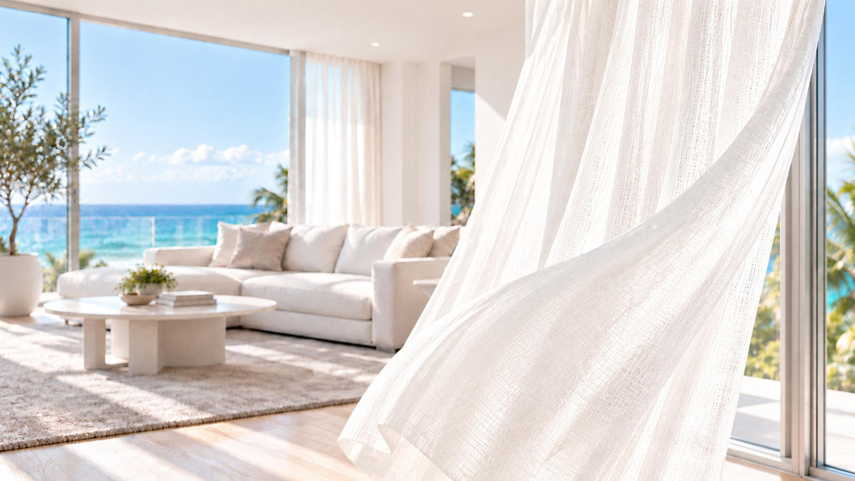 White sheer curtain moving in the breeze beside an open window in a bright coastal living room