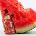 Watermelon Signature Scent oil bottle with pink oil leaning on a fresh watermelon slice