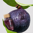 White Tea & Fig Signature Scent oil bottle with purple oil beside a ripe fig and fig leaves